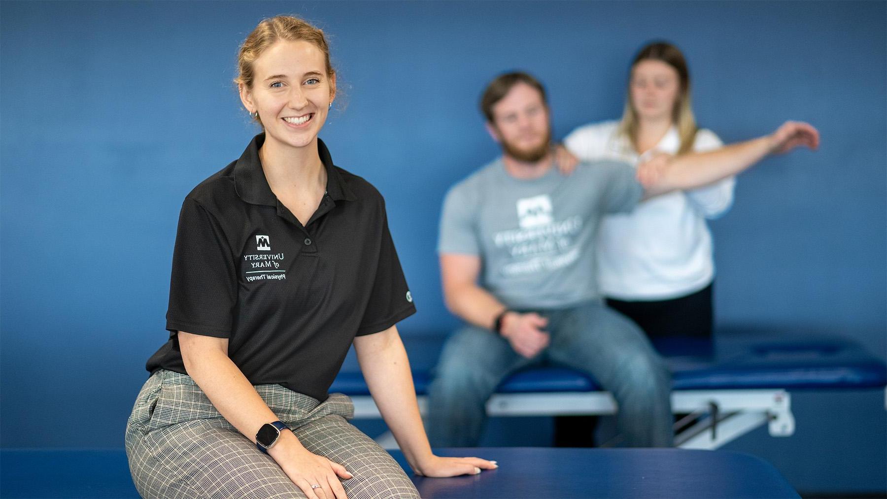 Student sitting in the forefront with a physical therapist working in the background.